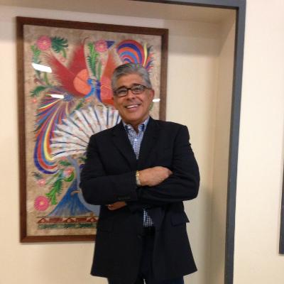 Photograph of Larry Rivas-Herrera-Cabrera standing in front of a painting, smiling with his arms crossed.